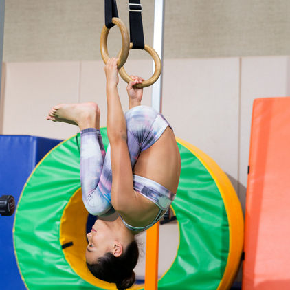 Young girl hanging upside down while holding onto gymnastics rings
