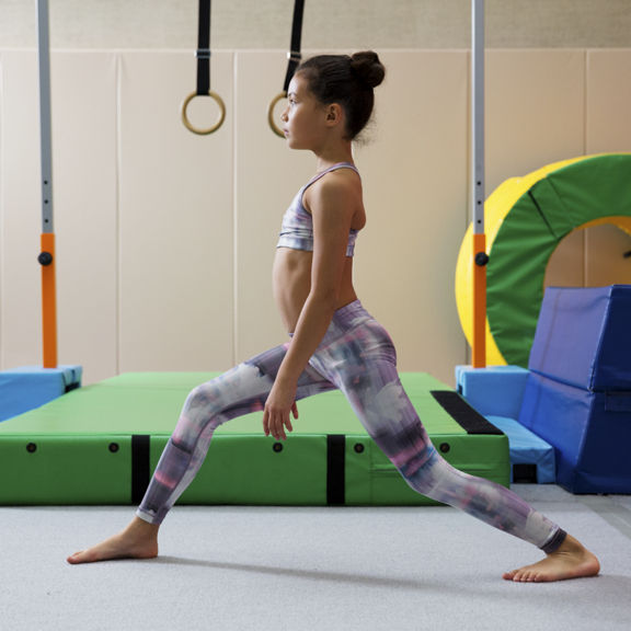A young girl in athletic clothing lunging forward in a tumbling studio