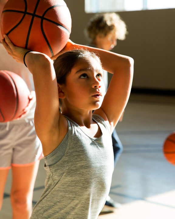 Close view of a female child holding a basketball above her head aiming at the basket