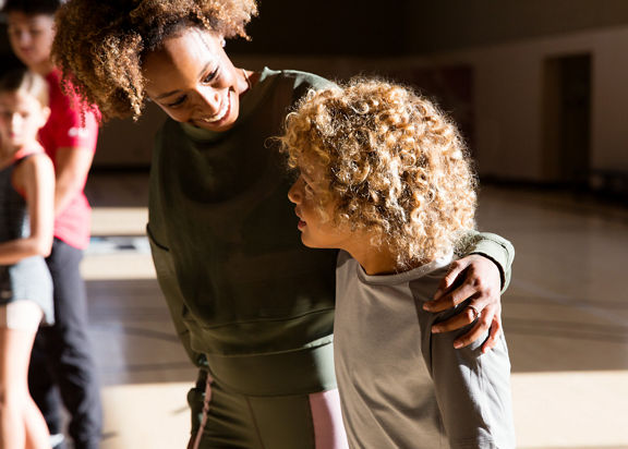 An adult female puts her arm around a male child in a gymnasium