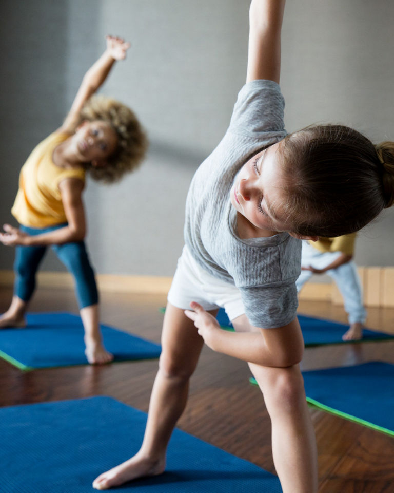 Young children bending over to the side, stretching, during a kids yoga class at Life Time