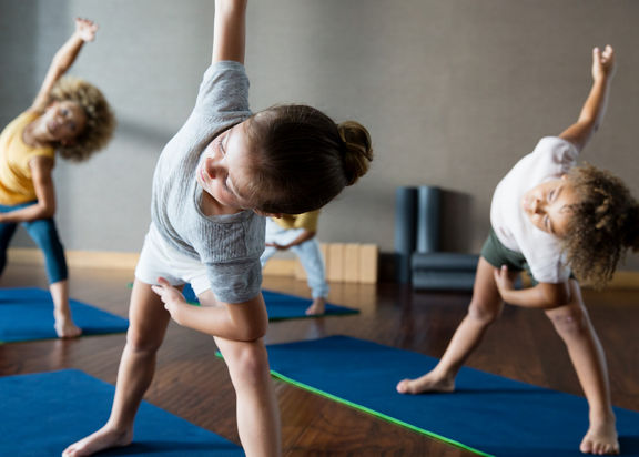 Young children bending over to the side, stretching, during a kids yoga class at Life Time