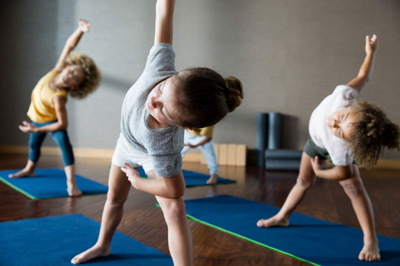 Young children bending over to the side, stretching, during a kids yoga class at Life Time