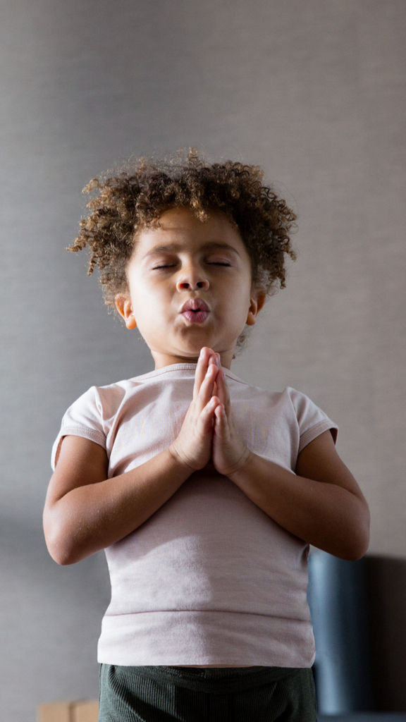 A young girl standing with hands in prayer pose with eyes closed during a kids yoga class at Life Time