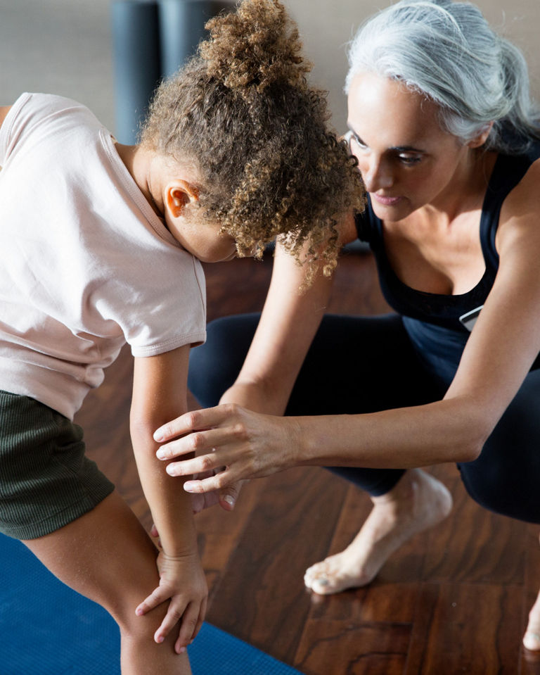 A yoga teacher helping a female child stretch on a yoga mat in a yoga studio