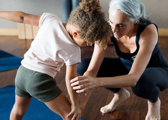 A yoga teacher helping a female child stretch on a yoga mat in a yoga studio