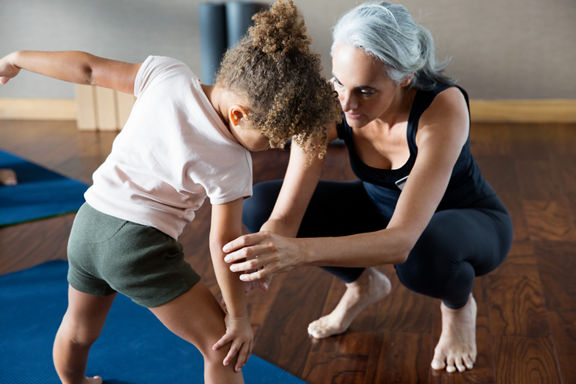 A yoga teacher helping a female child stretch on a yoga mat in a yoga studio