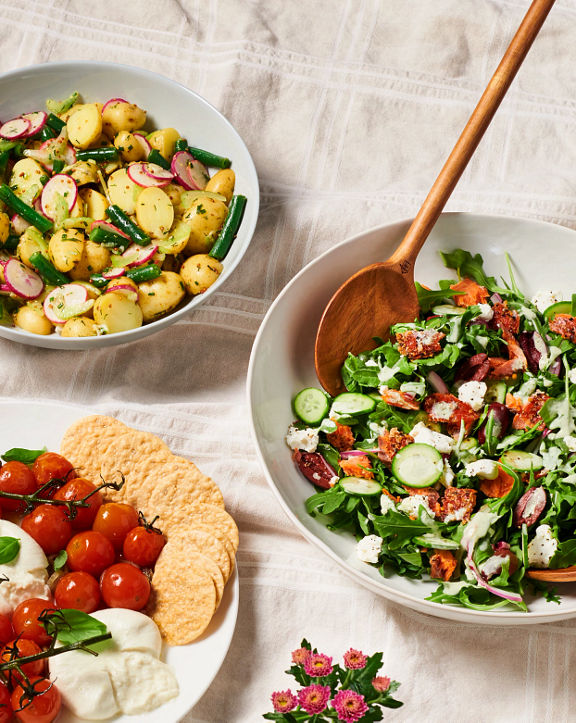 An indoor picnic set up with two veggies salads, one with salmon and peaches and cream sitting on a cream table cloth.