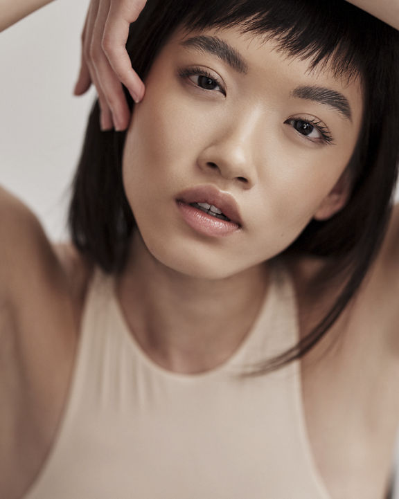 A close-up portrait of an attractive black-haired female with bangs and flawless skin