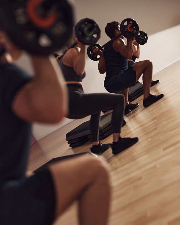 Four people squatting with barbells across shoulders during a Lift strength class at Life Time