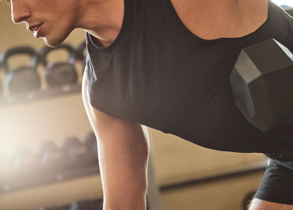 An adult male leaning over a step bench while exercising with weights