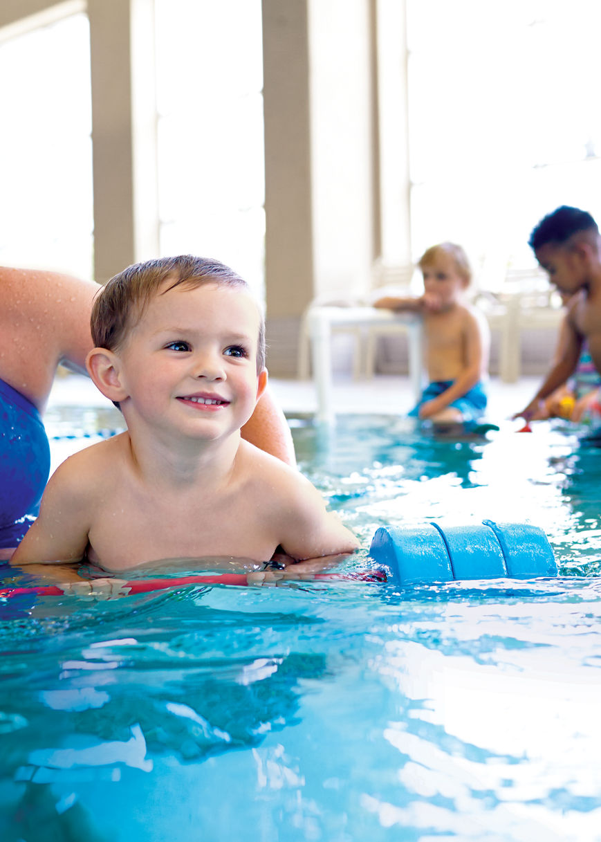 A group of children at a swimming lesson in an indoor pool with a Life Time swim instructor