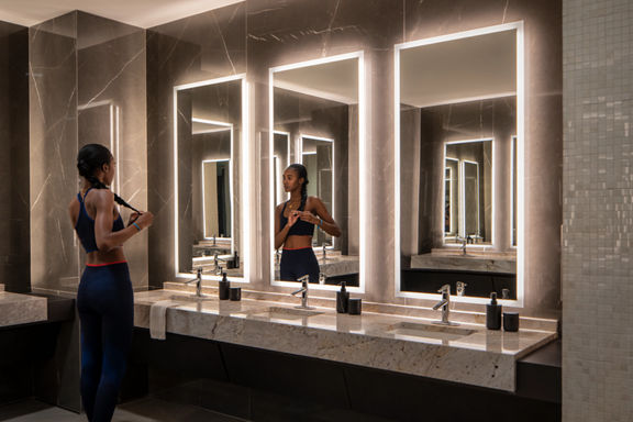 A female braiding her hair while looking into a mirror in the Life Time locker room