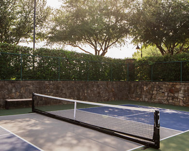 An outdoor pickleball court surrounded by a stone wall and tall trees