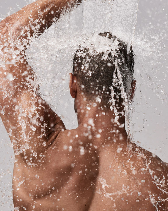 The back of a male body being showered with water