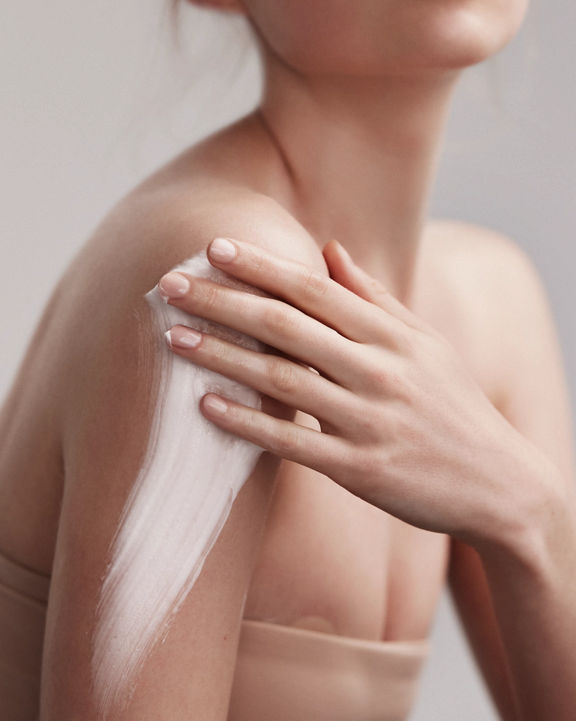 Portrait of an attractive female with flawless skin smearing lotion on her shoulder and arm