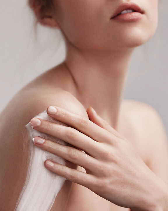 Portrait of an attractive female with flawless skin smearing lotion on her shoulder and arm