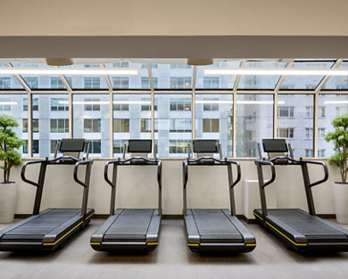 Row of treadmills facing windows leading out to an urban setting