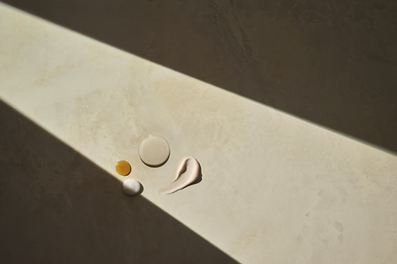 A variety of oils and lotions smeared on top of a cream marbled countertop