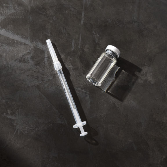 A syringe and clear glass vial on top of a dark gray background