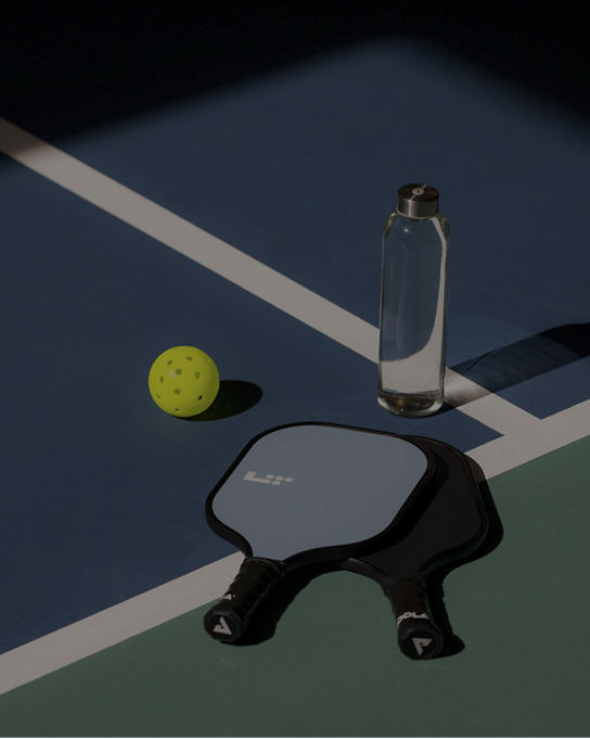 a pickleball, paddle and water bottle sitting on a pickleball court
