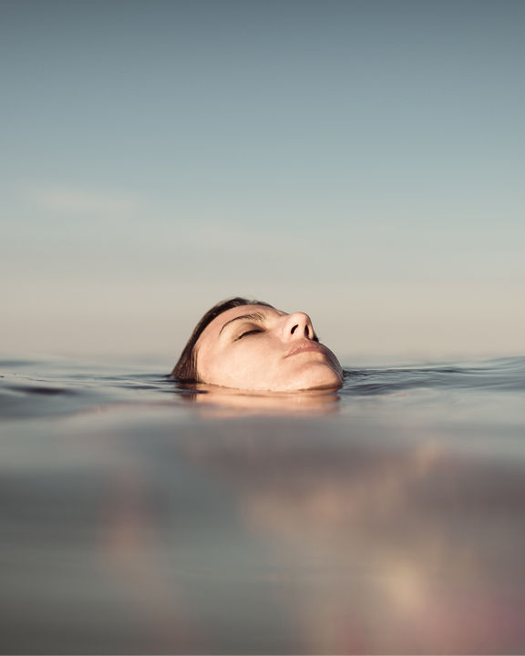 Peaceful portrait of a young beautiful woman floating on the sea and enjoying the relaxed sensation of the moment