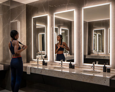 A female braiding her hair while looking into a mirror in the Life Time One Wall locker room