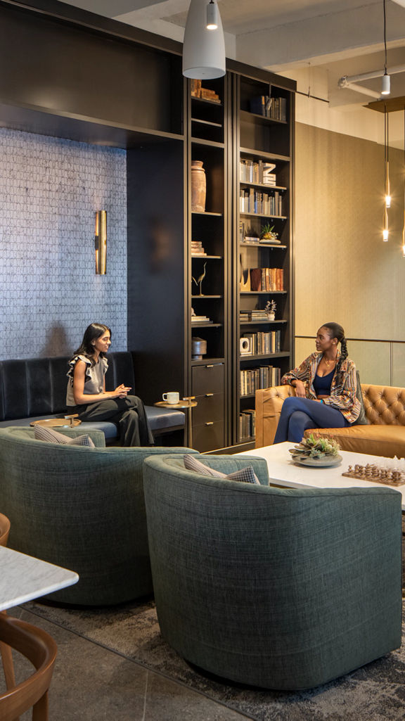 Two women sitting and conversing in a lounge area at the Life Time One Wall location