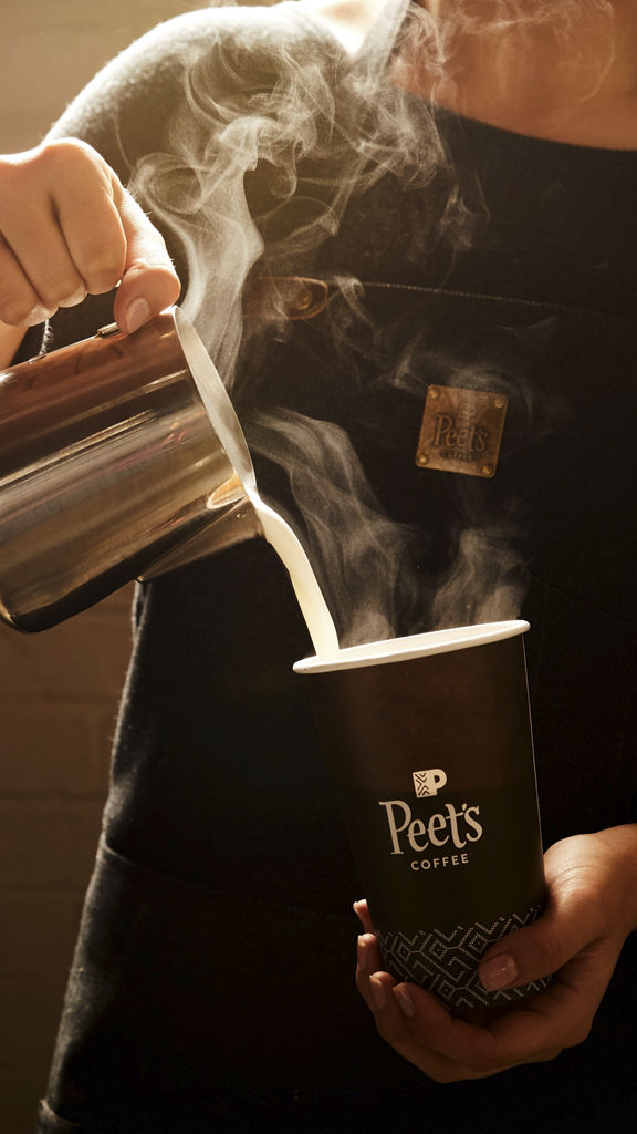 A barista pours steamed milk into a Peet's coffee cup