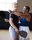 A man and a woman each holding a pickleball racuqet about to embrace eachother while standing on an indoor pickleball court