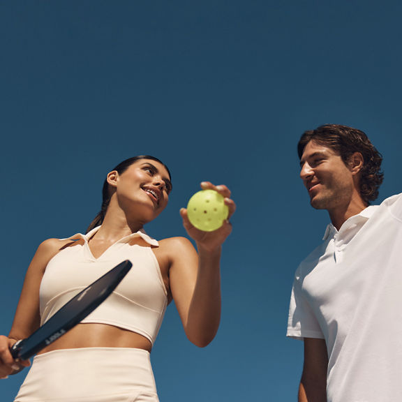 Two pickleball players looking at each other while holding a ball and paddle