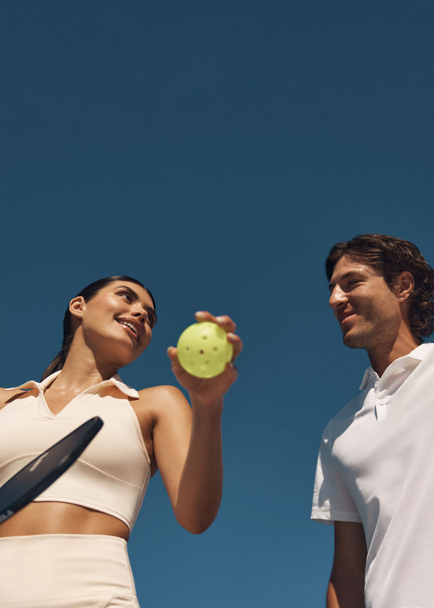 Two pickleball players looking at each other while holding a ball and paddle