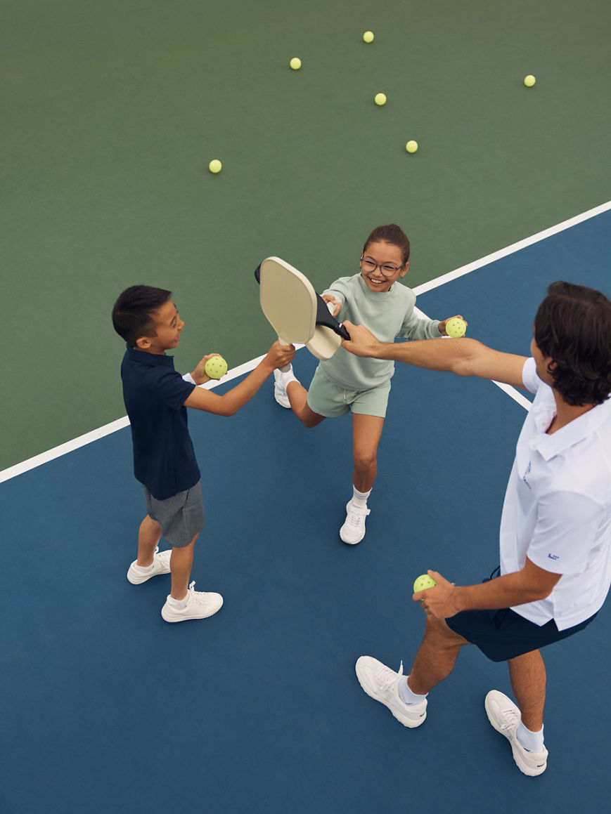 Two kids smiling on a pickleball court with a Life Time instructor