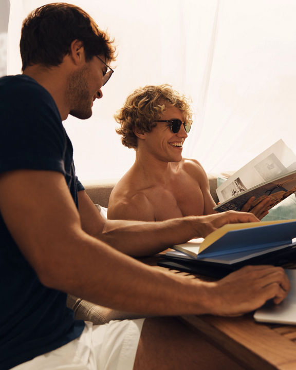 Two males relaxing in a poolside cabana and looking at books