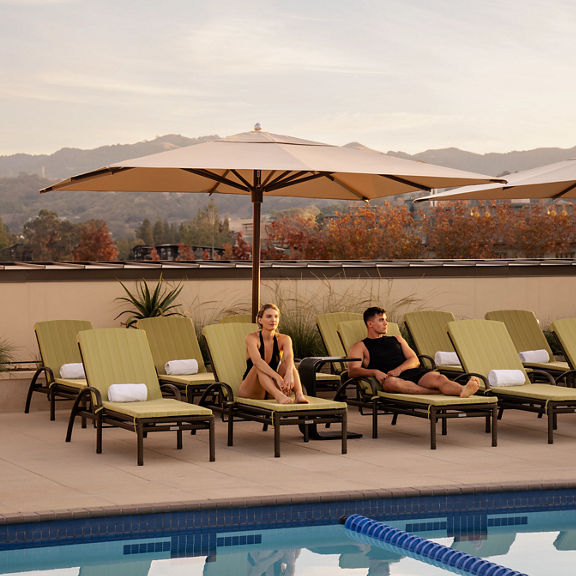 a man and woman sit on lounge chairs by an outdoor pool