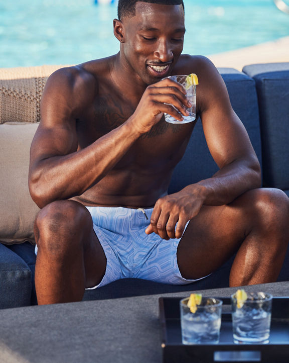 a man and woman share drinks on pool side sofas