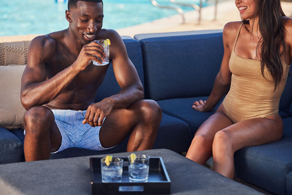 a man and woman share drinks on pool side sofas