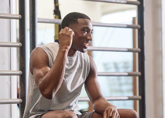 Portrait of an adult male sitting on the edge of an Outrace training device putting in ear buds