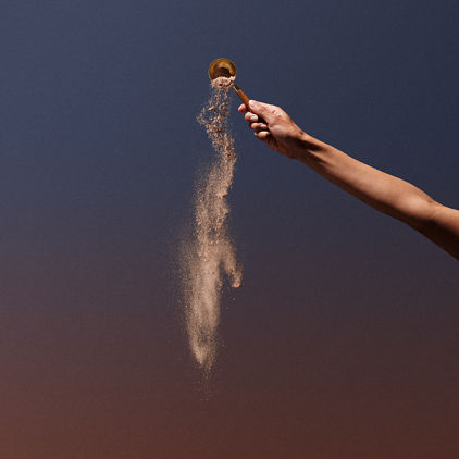 A female hand dumping out brown protein powder out of a metal scoop
