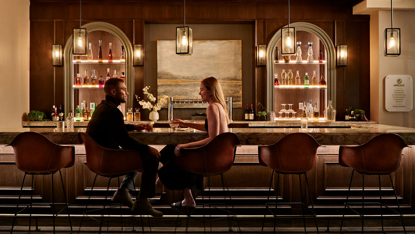 A couple sitting at the bar in deep conversation while drinking alcohol beverages