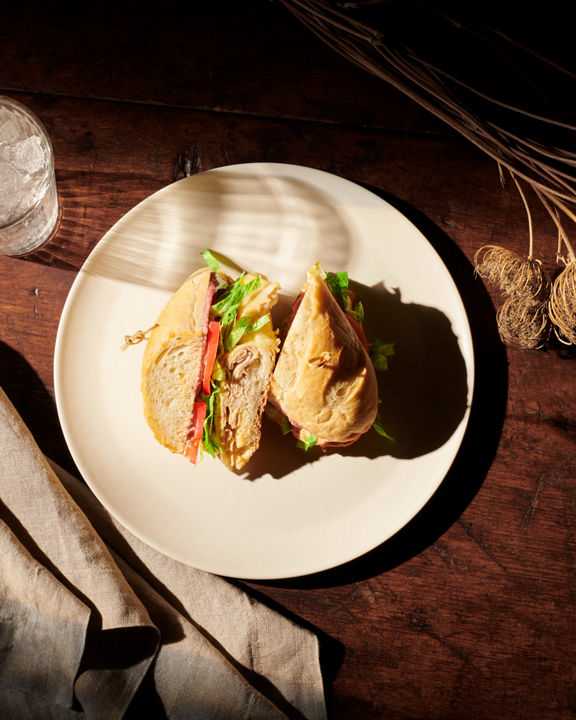 Overhead view of a turkey sandwich on a cream-colored plate placed on a dark wooden table with dried flowers and a glass of water