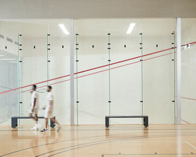 Two men walking by an open squash court at the Life Time South Austin club location