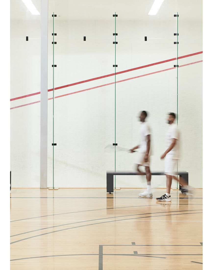 Two men walking by an open squash court at the Life Time South Austin club location