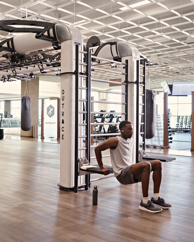 A man doing tricep dips on the edge of an outrace on an open fitness floor