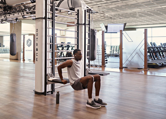 A man doing tricep dips on the edge of an outrace on an open fitness floor