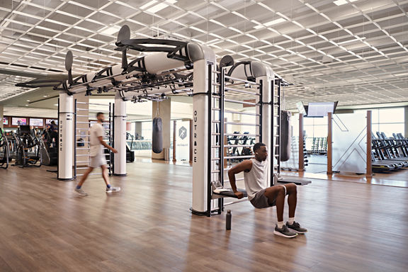 A man doing tricep dips on the edge of an outrace on an open fitness floor