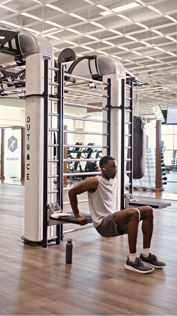 A man doing tricep dips on the edge of an outrace on an open fitness floor