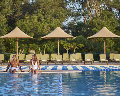 A man and woman smiling at each other while sitting poolside with their feet in the water