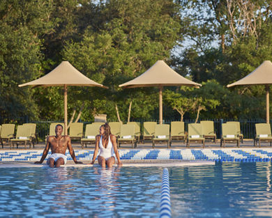 A man and woman smiling at each other while sitting poolside with their feet in the water