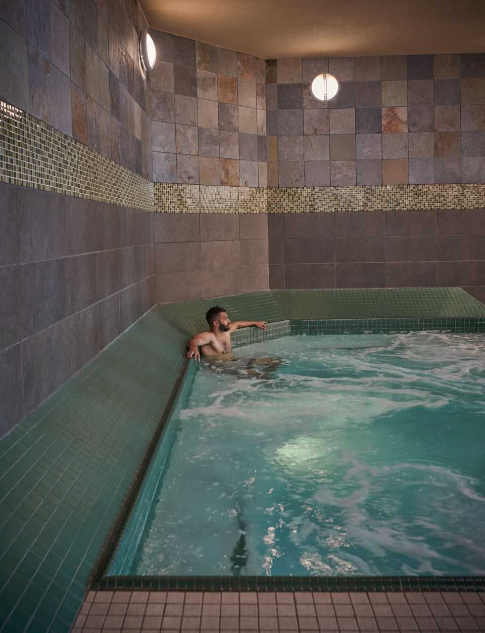 A man sitting and relaxing in an indoor whirlpool at the Life Time South Austin club location
